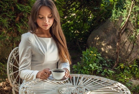 Brunette in white drinking coffee outdoors